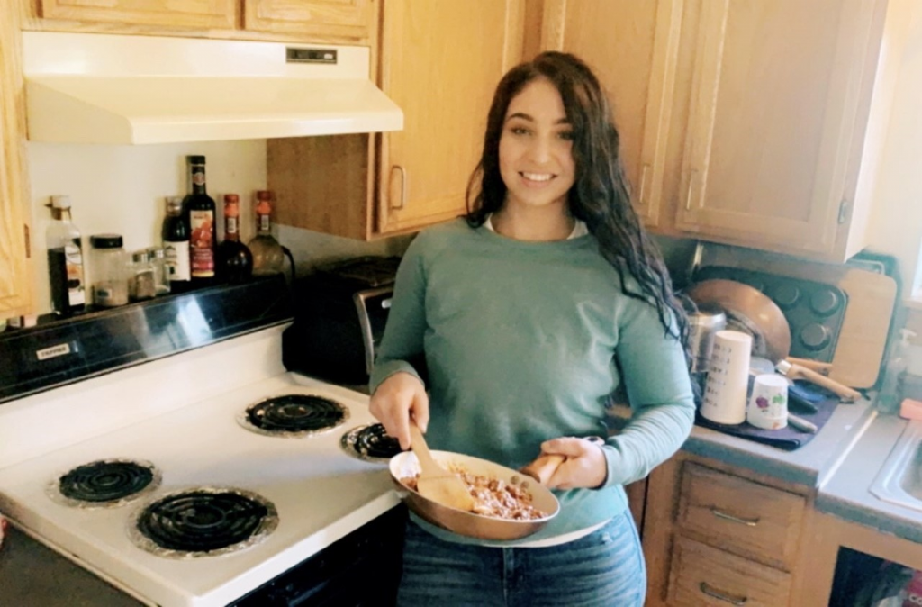 Alyssa smiles while stirring ravioli in a frying pan in her kitchen.