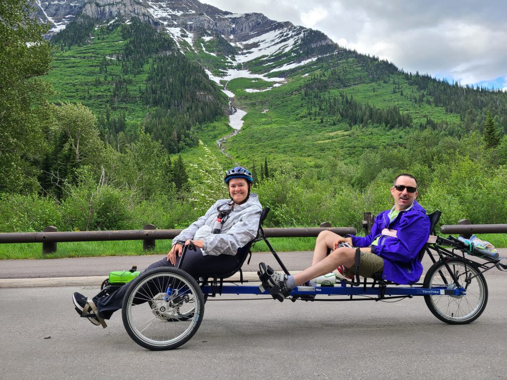 Peter and Sherene on the trike, a magnificent green, snow-capped mountain behind them
