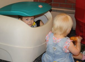 Little boy playing peek-a-boo from inside plastic trunk.