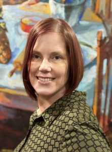 Headshot of Heidi Rabe. Heidi has shoulder-length straight red hair. She's smiling with a vibrant painting behind her.