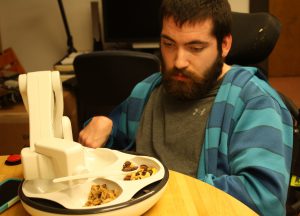 Devin waits while the Obi spoons up some trail mix. Obi is sleek, white design with robotic arm and four bowls set into a tray.