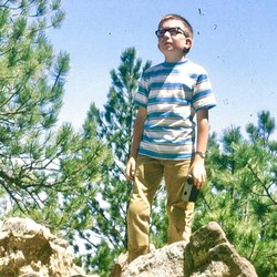Doug Doty, as a child, stands on a rock in the woods.