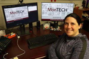 Michelle sits smiling at her desk with two computer monitors behind her showing a MonTECH Notetaking PowerPoint