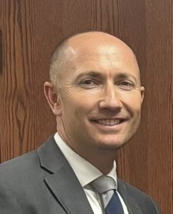 Head shot of a man in a jacket and tie, smiling. 
