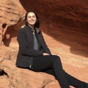 Young woman smiling, sitting in sun on red desert rock.