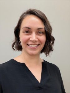 Head shot of Liz Kuehn. She is smiling, an attractive woman with black wavy hair cut just above her shoulders and a bright smile.