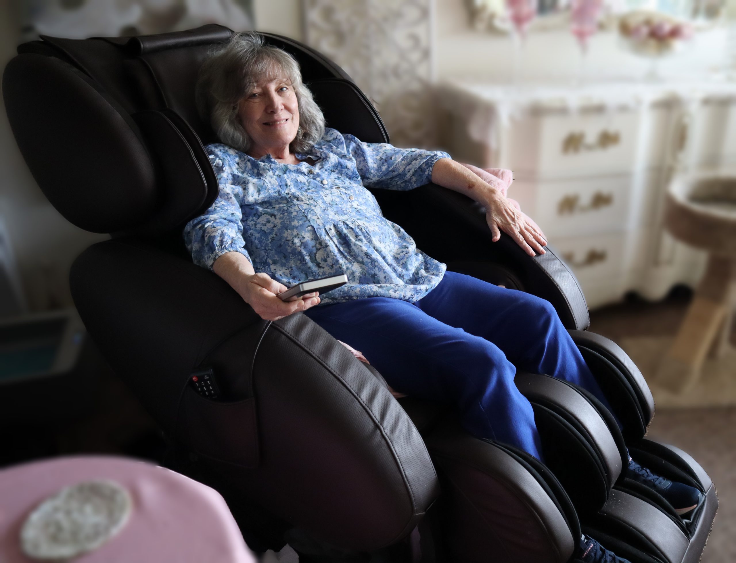 Older woman smiles from a large massage chair. Her lower legs are receiving pressure from the chair.