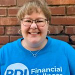 Close-up picture of a woman smiling, wearing a bright t-shirt with RDI's logo and print reading "Financial wellness."