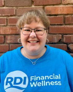 Close-up picture of a woman smiling, wearing a bright t-shirt with RDI's logo and print reading "Financial wellness."
