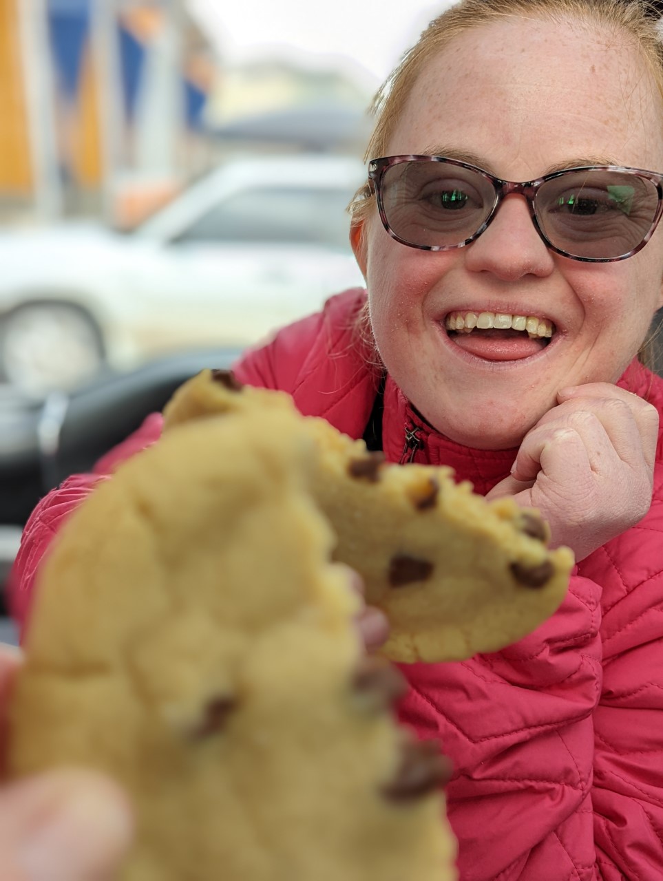 Young woman with Down syndrome smiles while toasting her mom with a chocolate chip cookie she baked at her new bakery job.