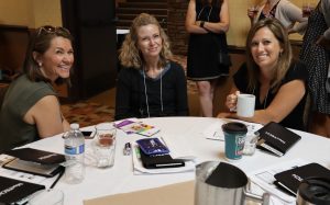 Three women smiling, sitting at a table at MontCOMM 2019