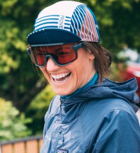 Close up of Maddy laughing big. She's wearing biking goggles and a bike hat.