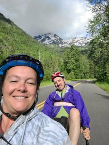 Sherene and Peter smile from their bike seats, a beautiful snowy mountain in the background.