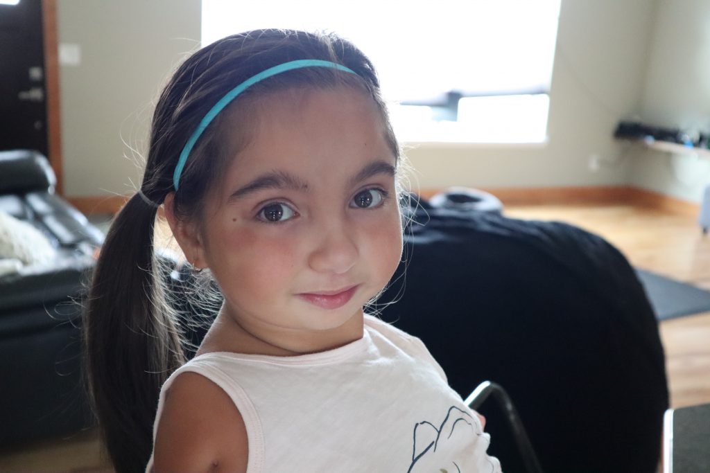 Close-up of Tenley's face. She is smiling, with big brown eyes, dark hair pulled back in ponytail, and a bright blue headband.