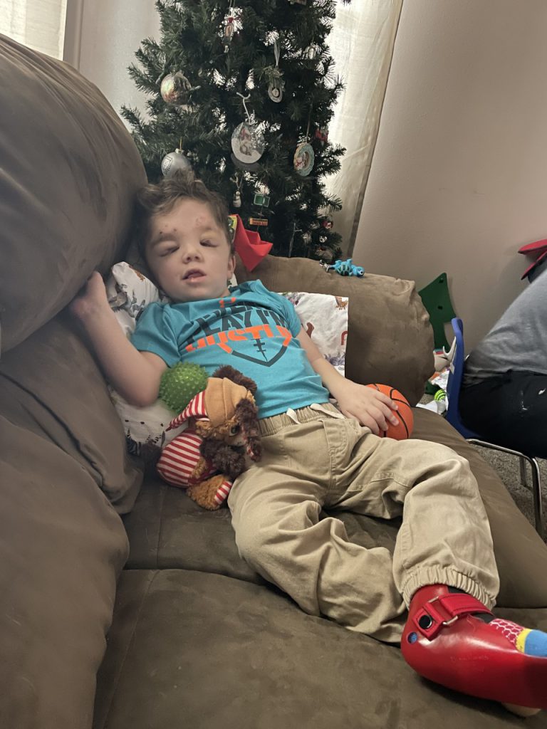 Little boy lays smiling on the couch with stuffed toys.