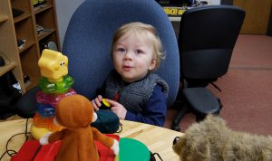 Blond toddler pushes button to make jack-in-the-box go, looking at camera saying ooooo.