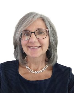 Close-up headshot of Dr. Carole Zangari. She has shoulder-length gray hair neatly framing her face. She smiles, wearing glasses, a black top, and a sparkling necklace.