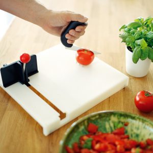Person using food prep board to hold tomato for one-handed slicing.