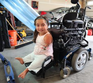 Tenley rides her vertical lift from her power chair's seat down to the floor.